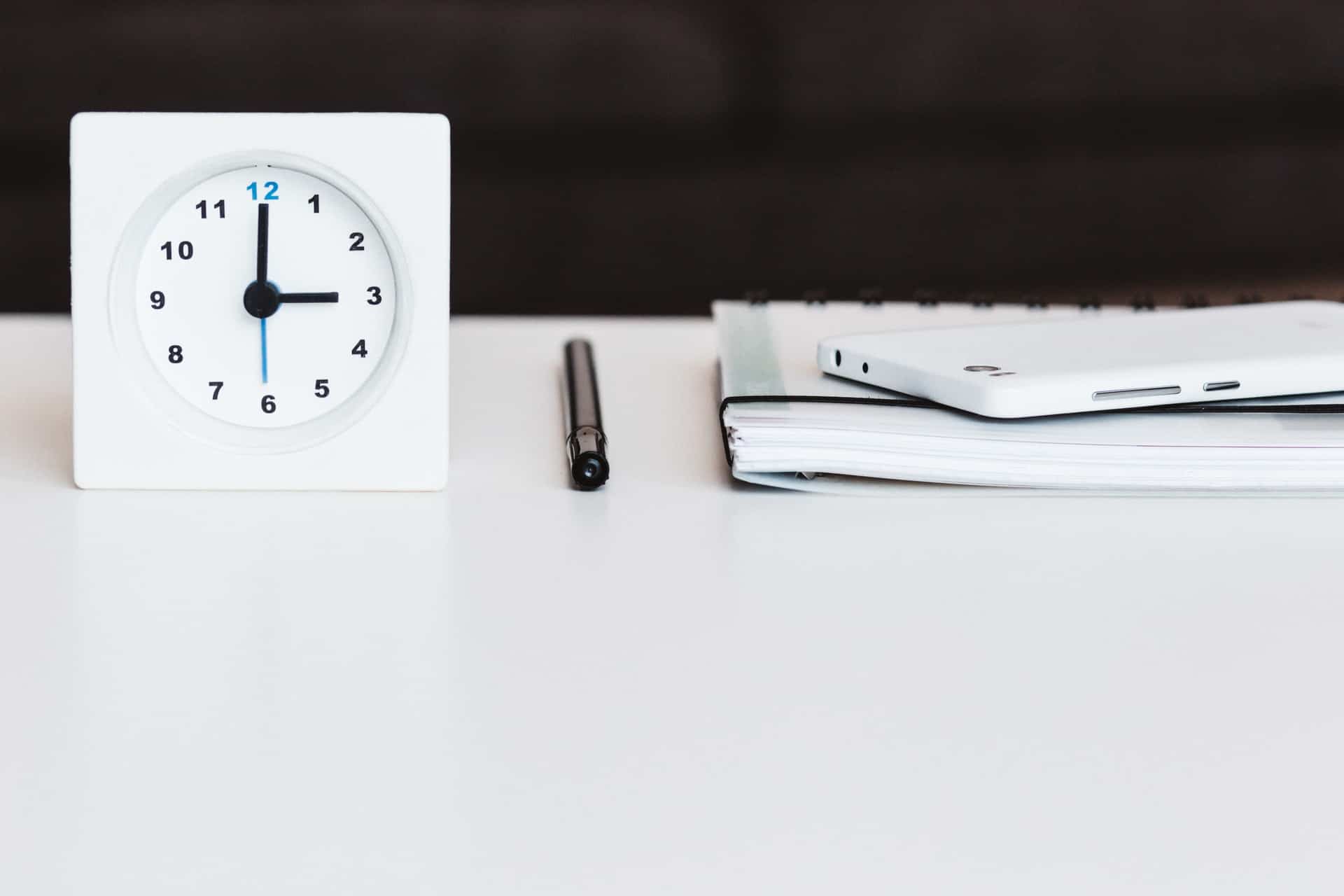 a clock, a pen, cell phone and a notepad organized for a writing session