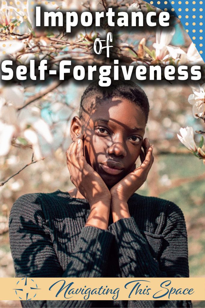 A black woman stands under a white flowers tree, posing with her hands around her face - Importance of self-forgiveness