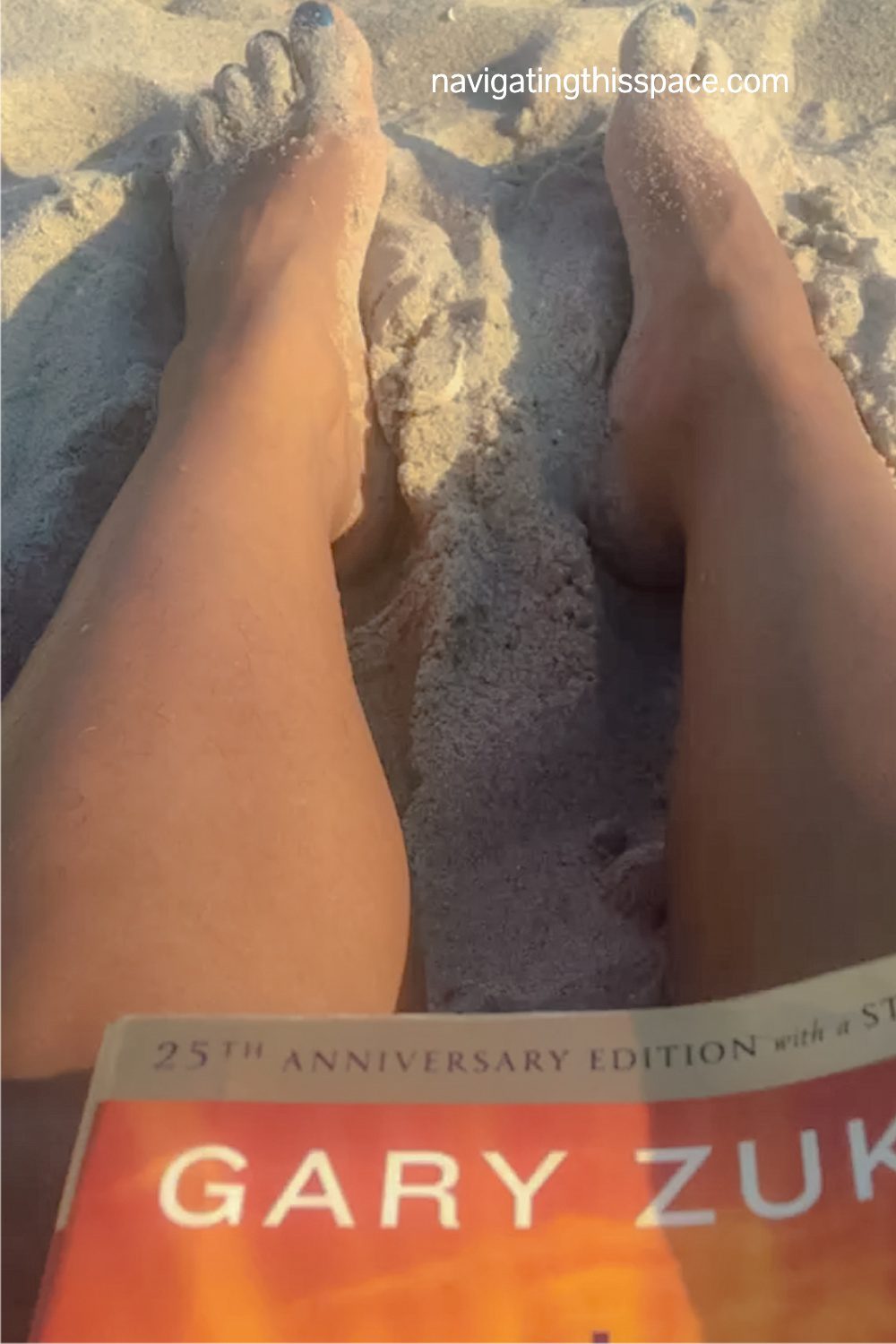 Legs on the sand reading Gary Zukav book The Seat Of The Soul