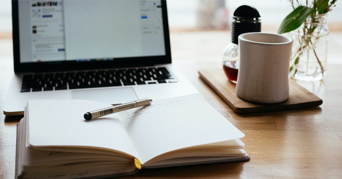 a blank open notebook sitting on a desk in front of a computer