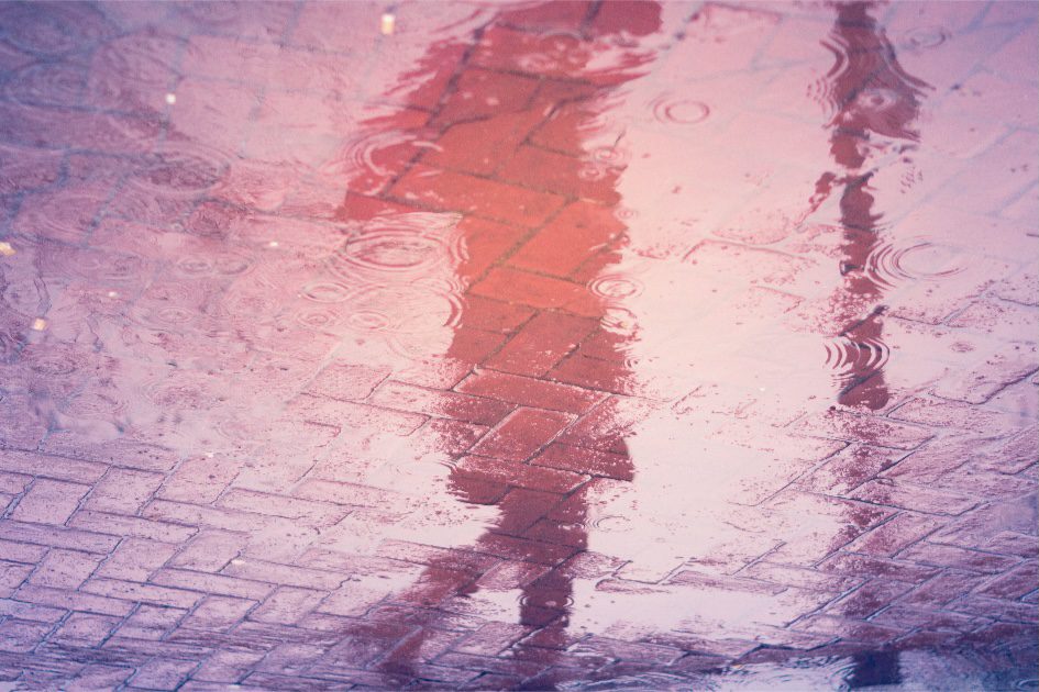 the water reflection of a shadow figure walking alone under an umbrella on a rainy night