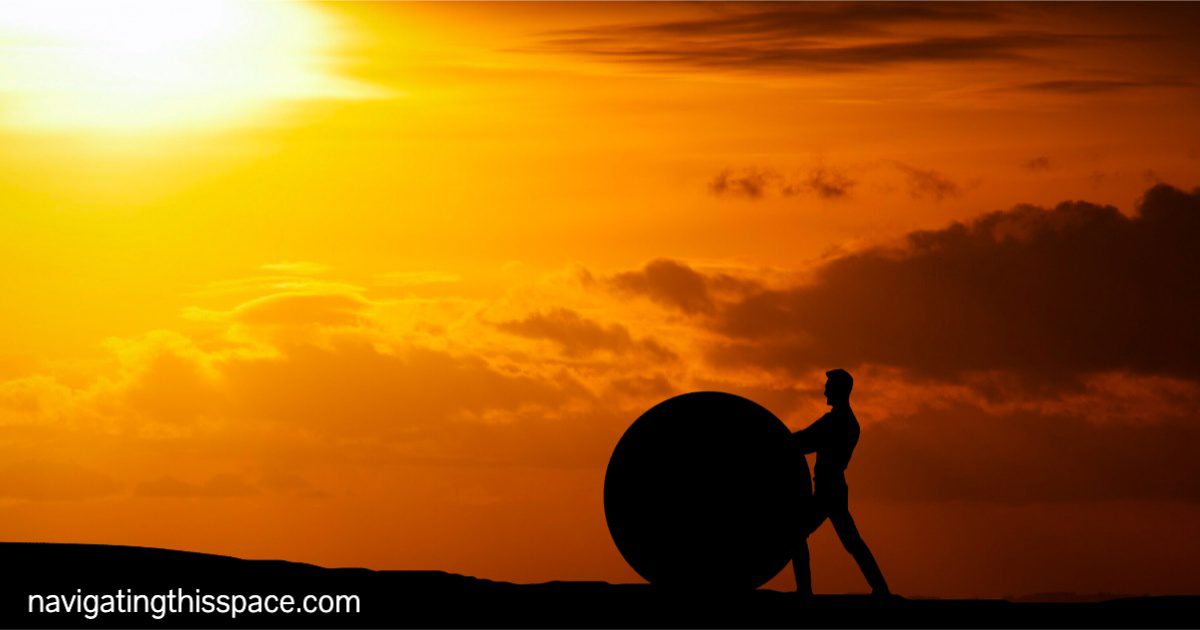 a figure pushing a rock on a rocky pavement during the sunset