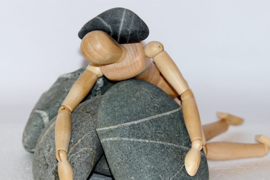 a wooden figure burden down by piles of rock representing how the struggles of life can get you down