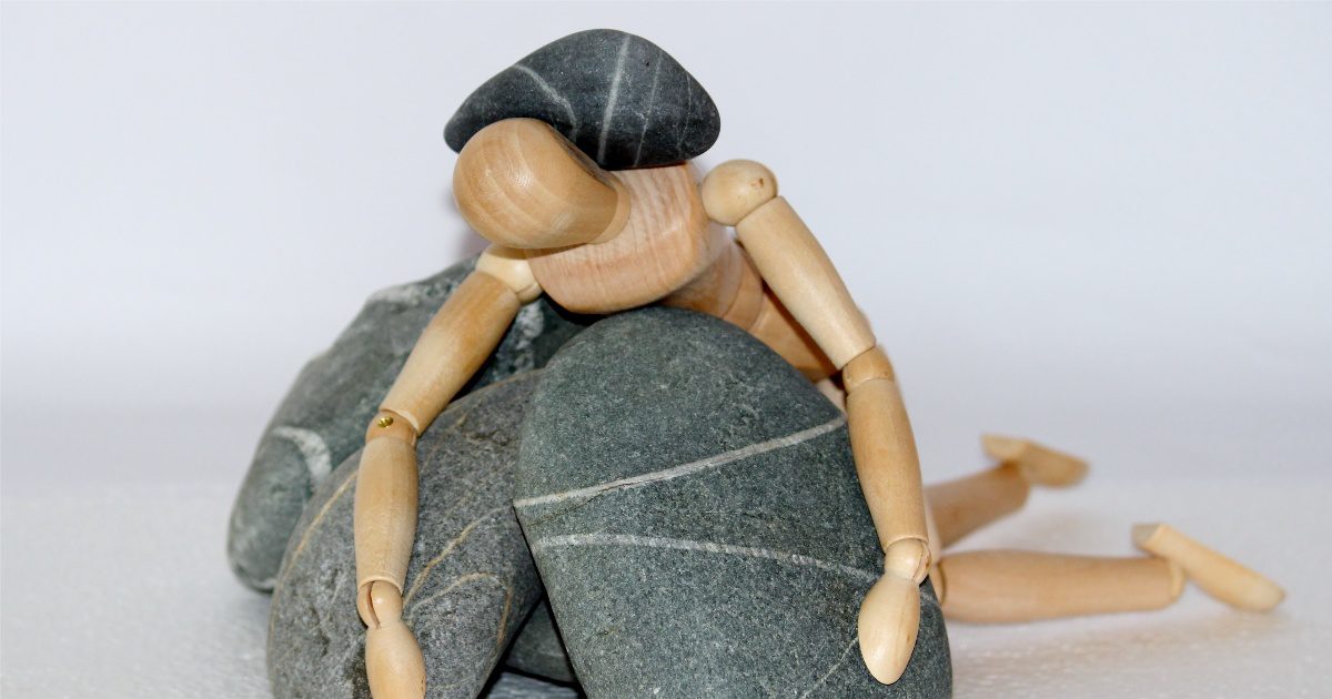a wooden figure burden down by piles of rock representing how the struggles of life can get you down