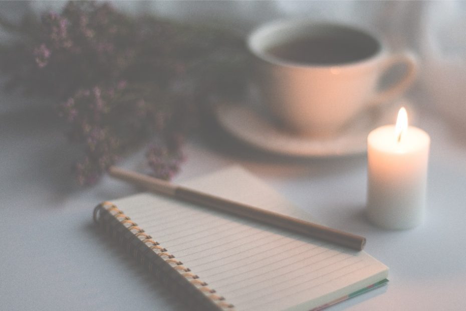 a notebook, lit candle and a cup of tea ready to write journaling goals