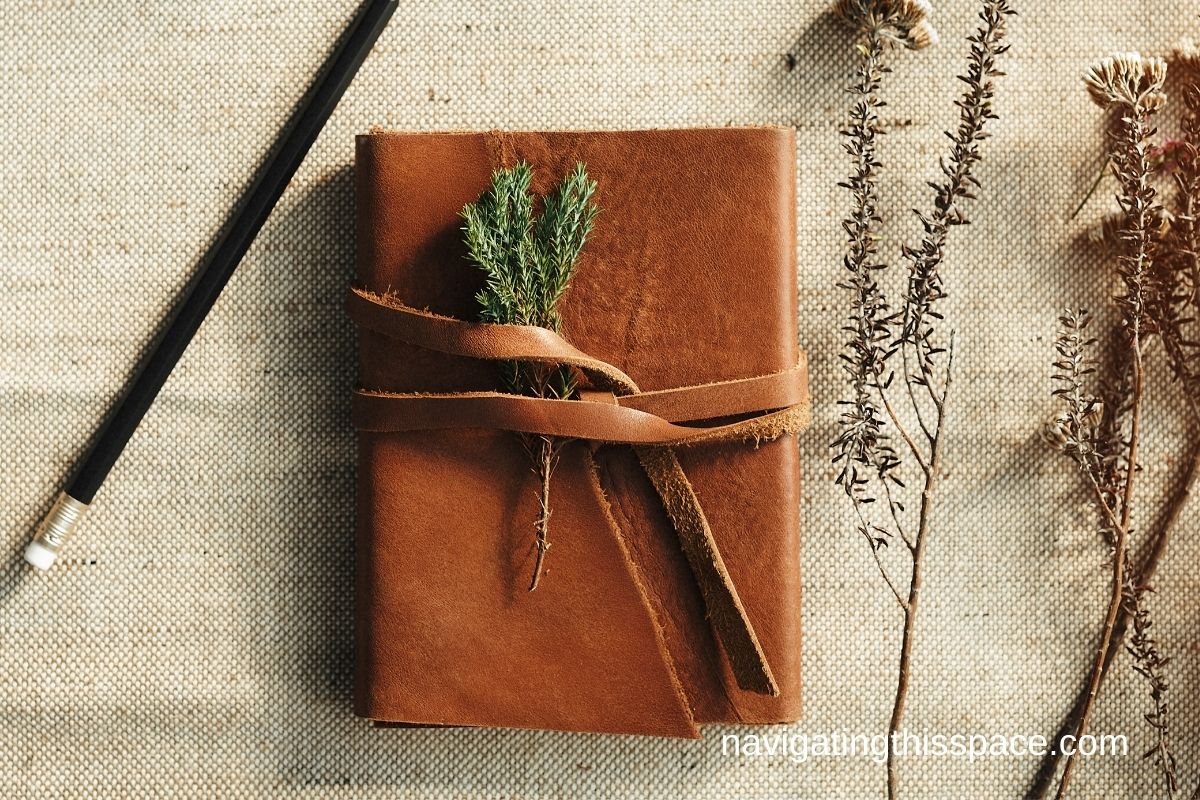 A leather bound Journal notebook with a pencil and dried flowers on a cloth