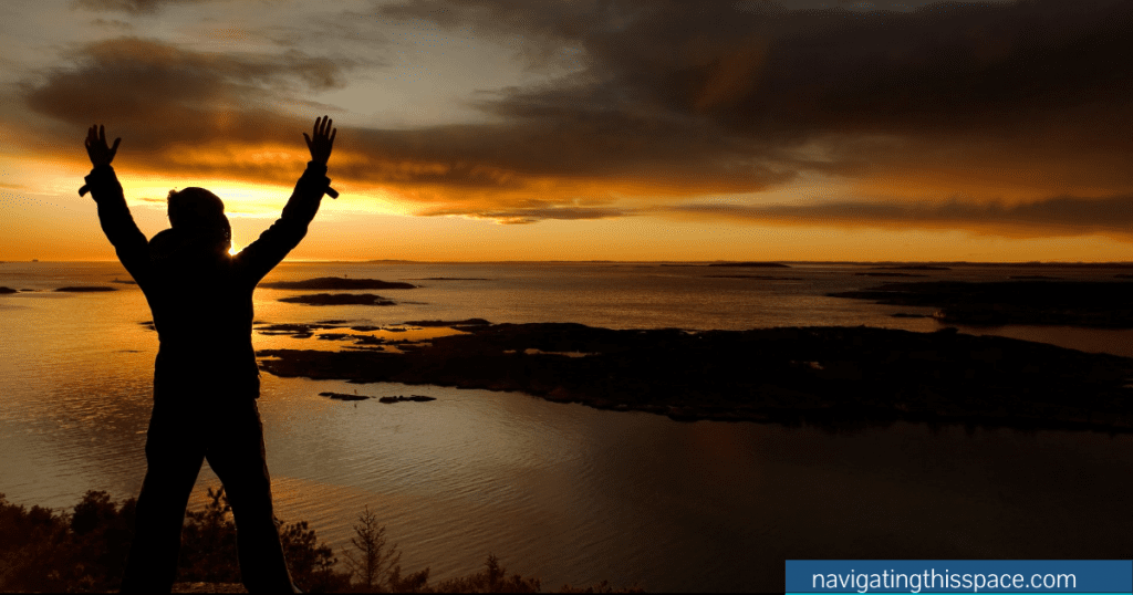 A silhouette on the beach at sunset with both hands raised in celebration