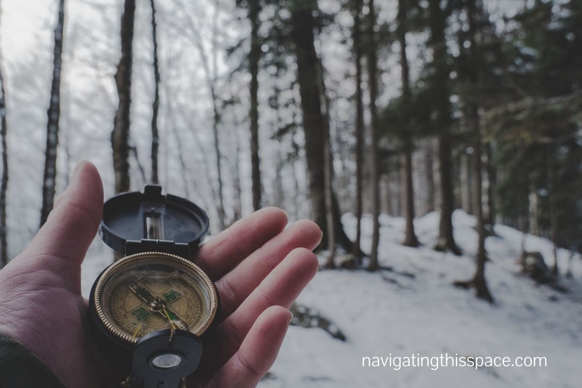 a hand holding a compass in the snowy woods